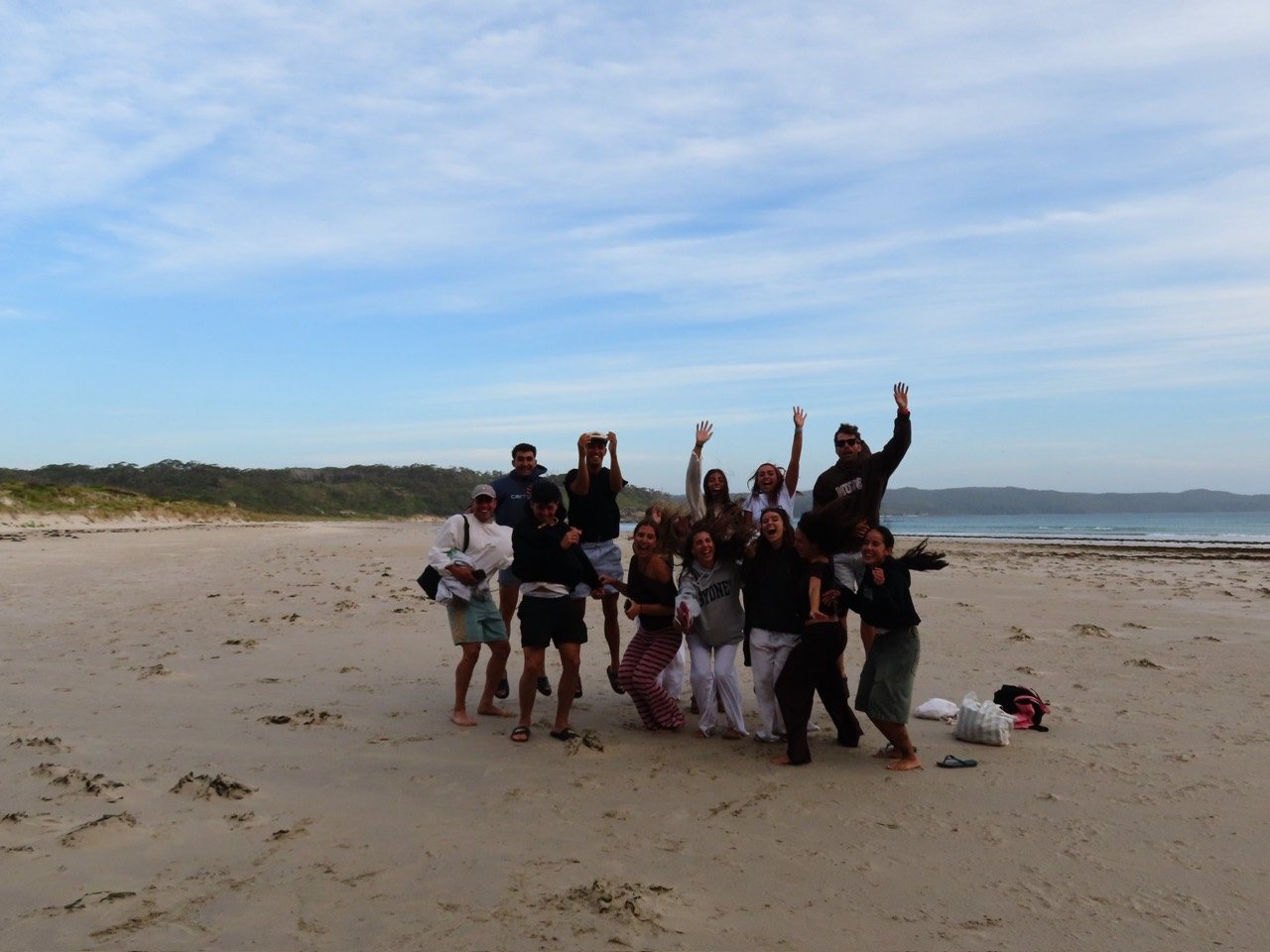 A group of friends smile and raise their arms on the beach