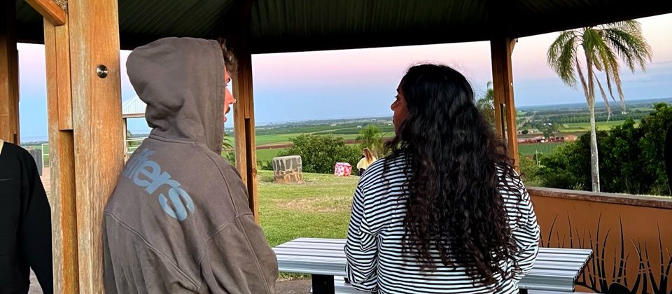 Pablo in a grey hoodie and a friend look out at the landscape, seen from behind