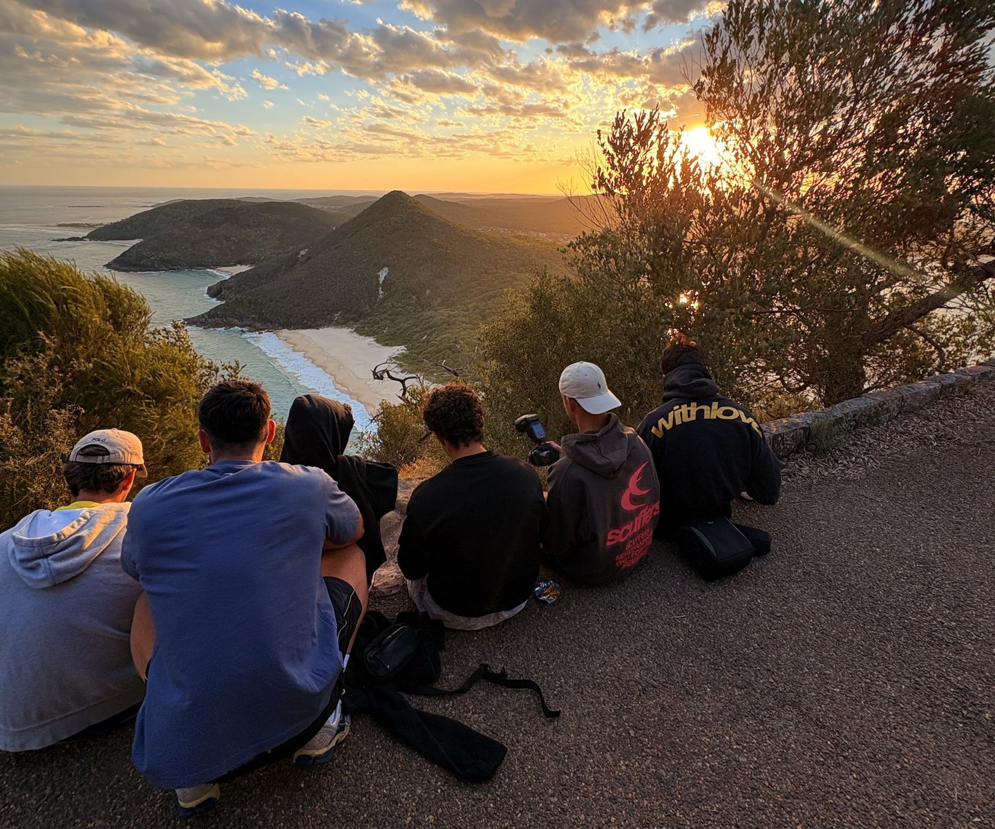 Friends sitting at a lookout share a sunset by the sea